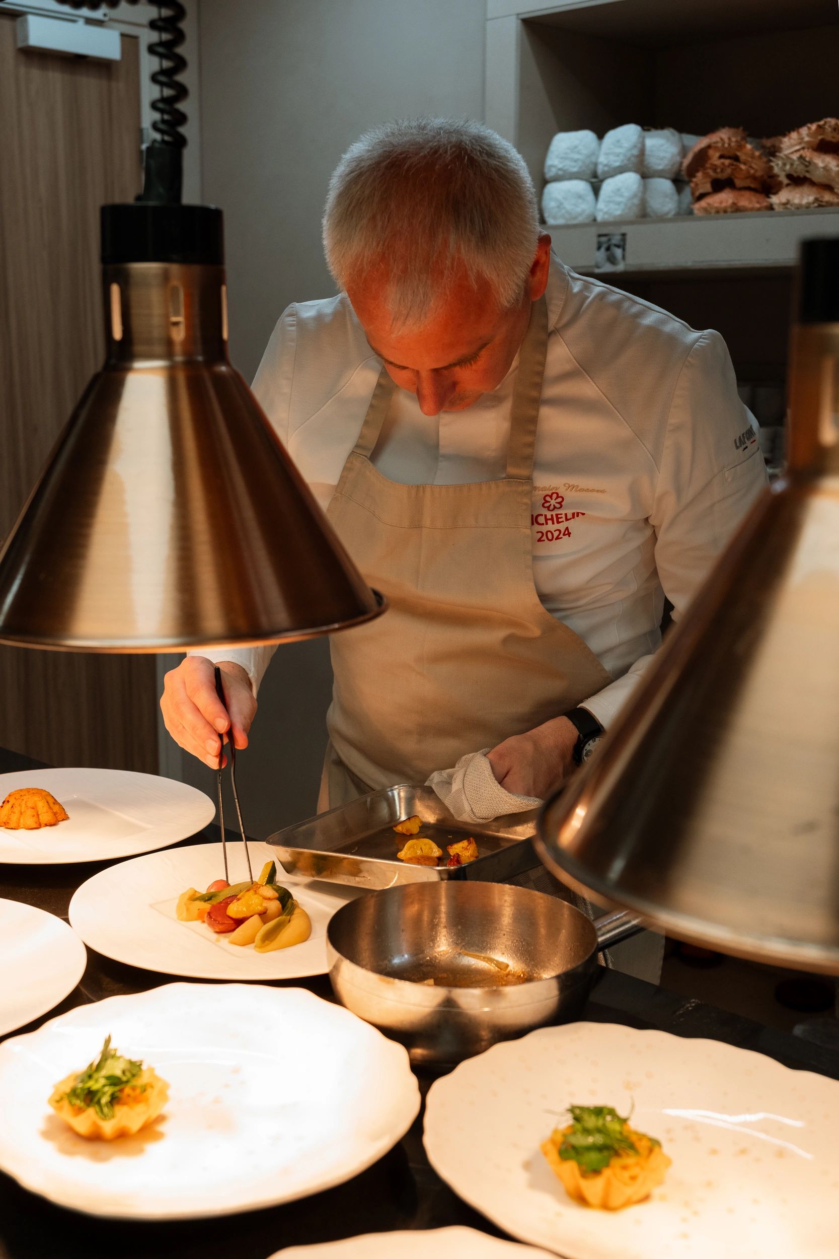 Chef Michelin prépare un plat gastronomique avec lampe chauffante en cuisine professionnelle