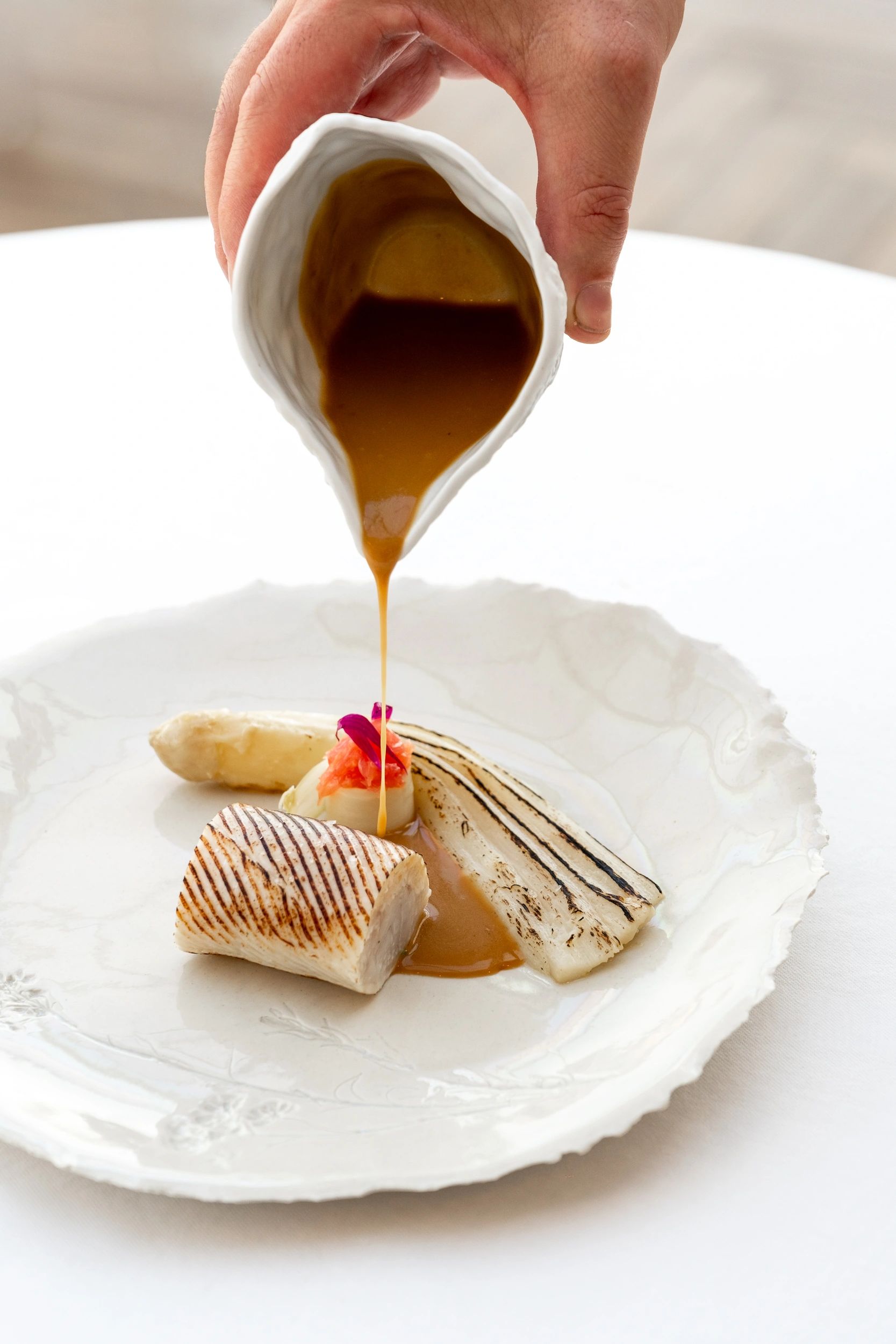 Chef versant une sauce dorée sur un poisson grillé garni de légumes dans une assiette blanche