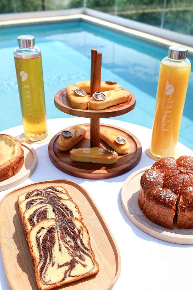 Plateau de pâtisseries et boissons au bord d'une piscine avec brioches, pain aux raisins et jus de fruits frais